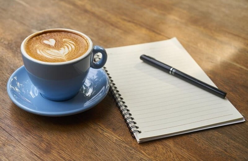 A cup of coffee a notebook and a pen on a table