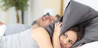 Man snoring while his wife is covering ears with the pillow